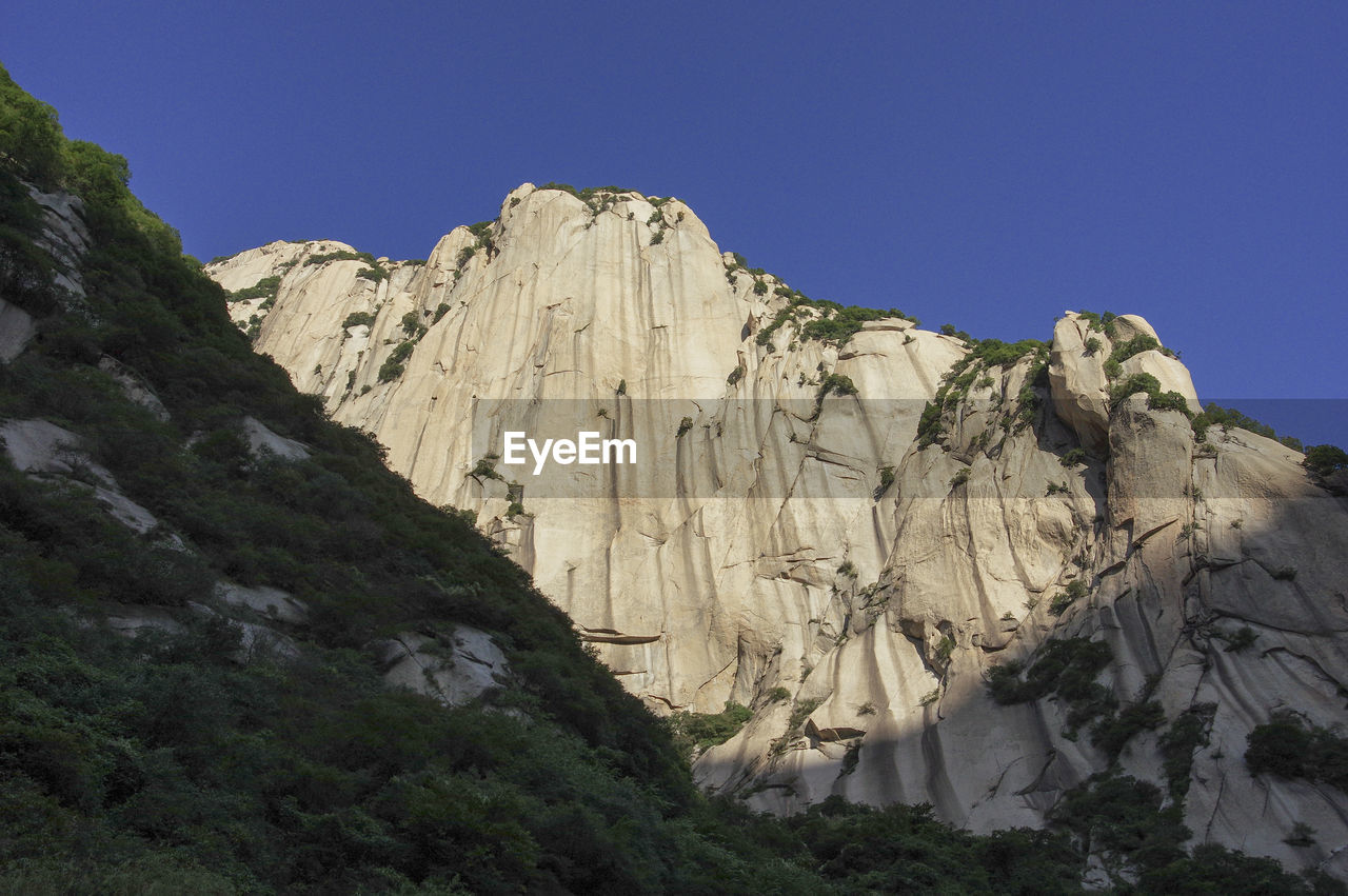 Low angle view of rocky mountain against clear blue sky