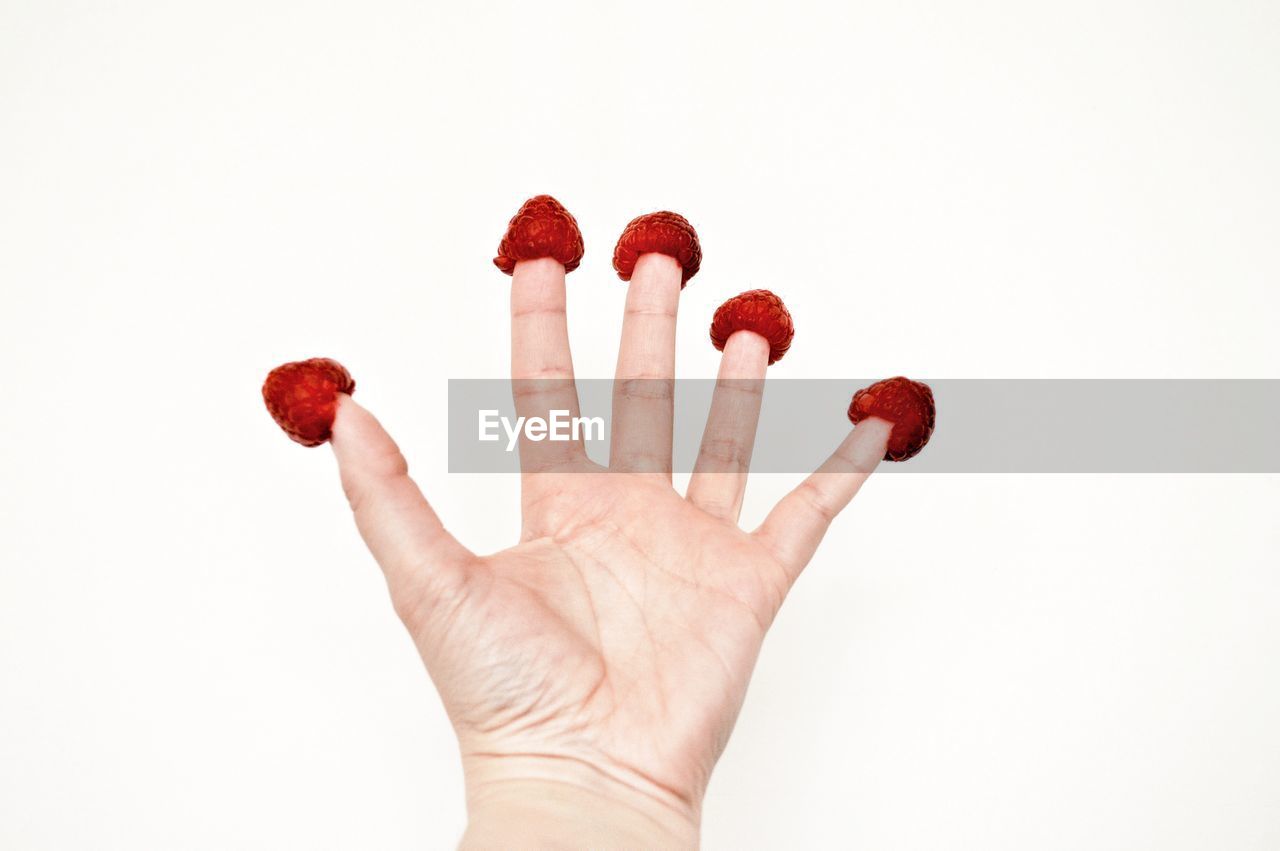 CROPPED IMAGE OF HAND HOLDING STRAWBERRY OVER WHITE BACKGROUND
