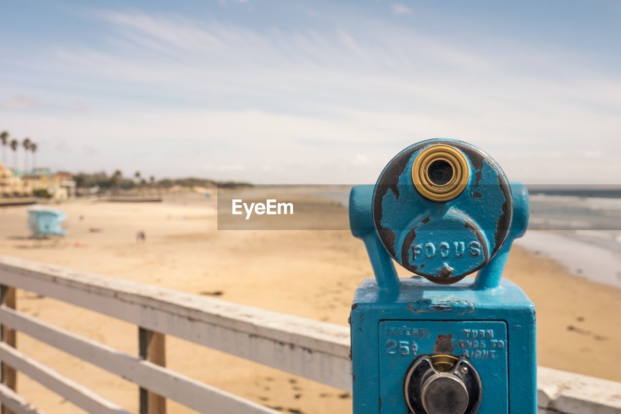 Coin-operated binocular on pier at sandy beach against sky