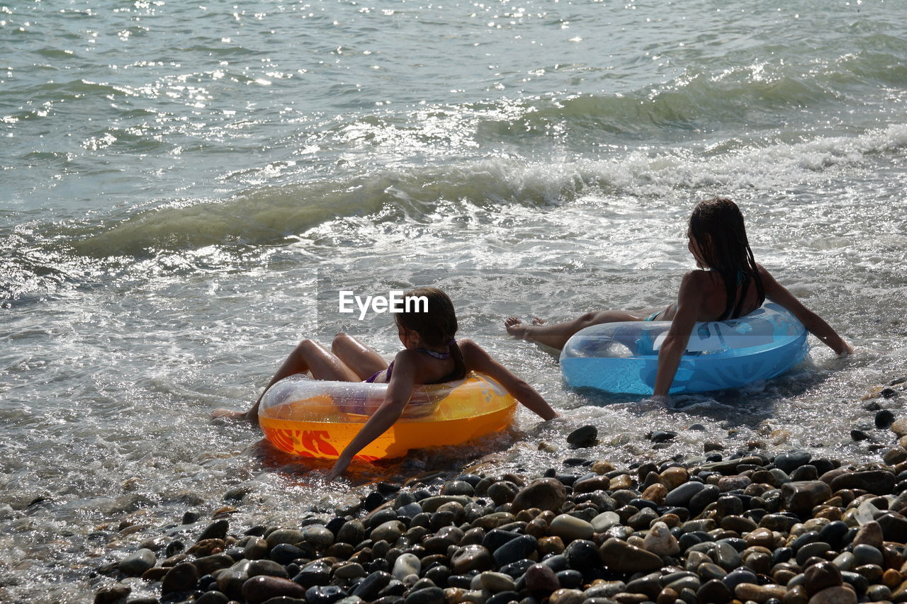 Rear view of people sitting in inflatable ring on beach