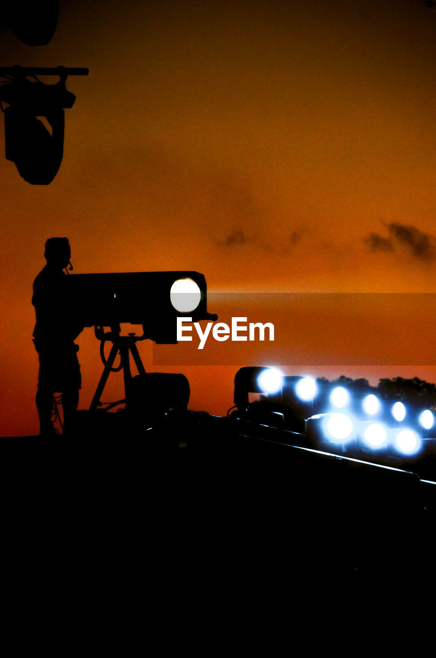 Silhouette man standing by illuminated lighting equipment at sunset