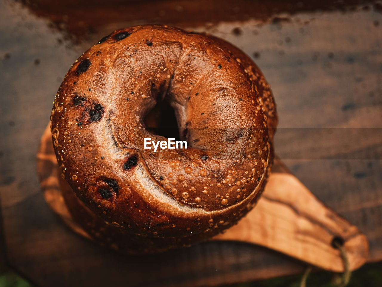 Above view of stack of three blueberry bagels on small olive wood cutting board