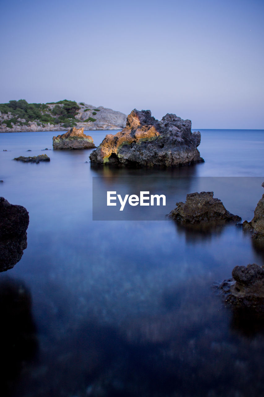 Rock formations in sea against clear blue sky