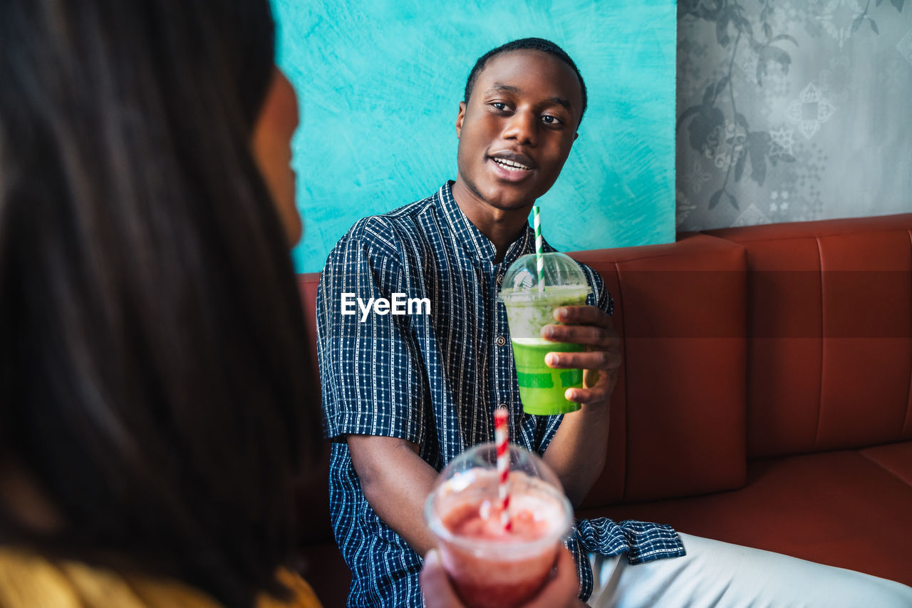 Content young female with glass of smoothie talking to ethnic partner at table with healthy food