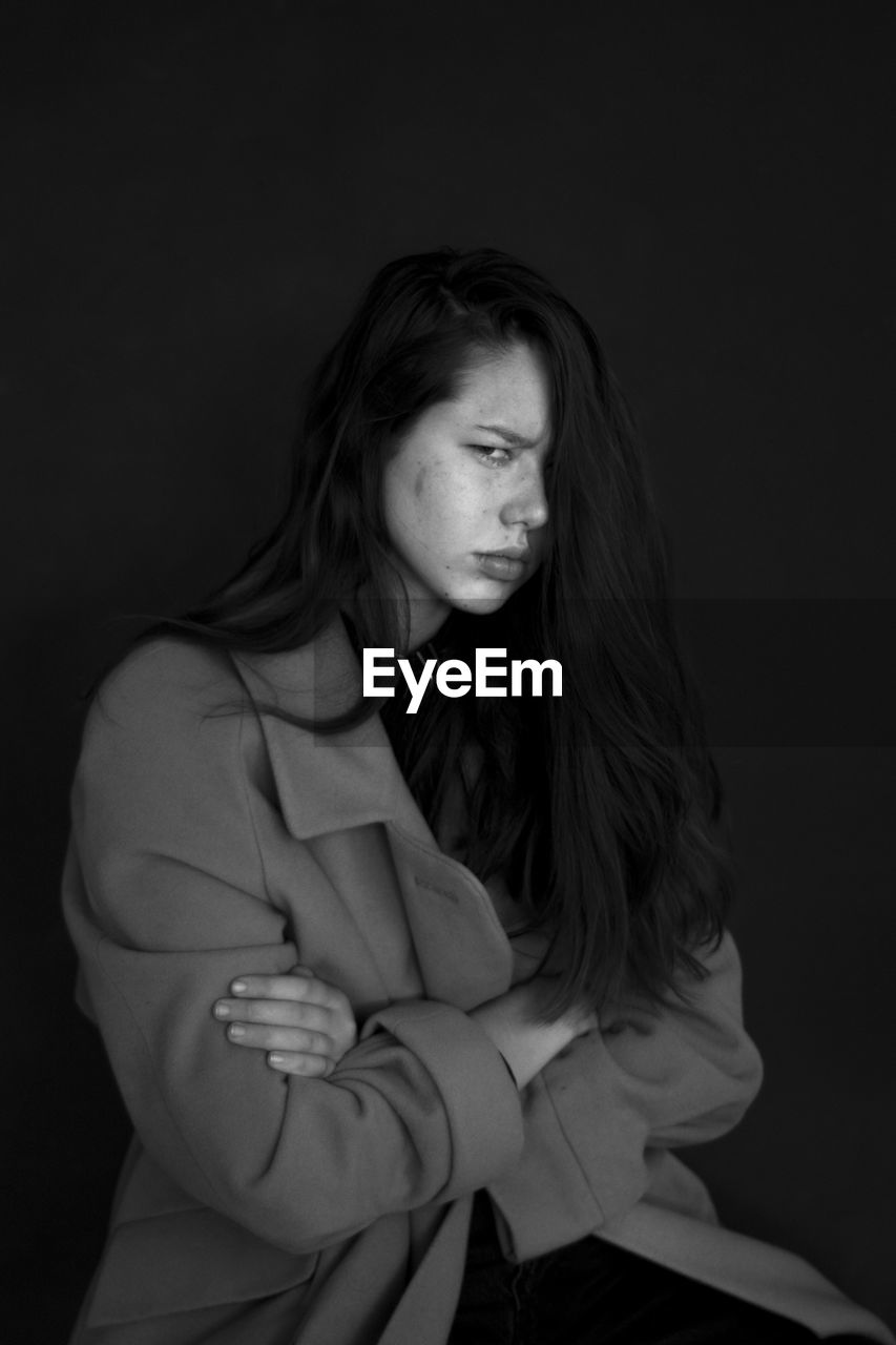 Portrait of angry woman sitting against black background