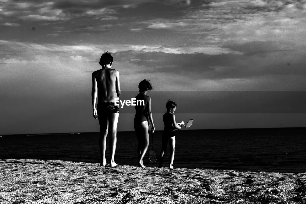 FRIENDS STANDING ON BEACH AGAINST SEA