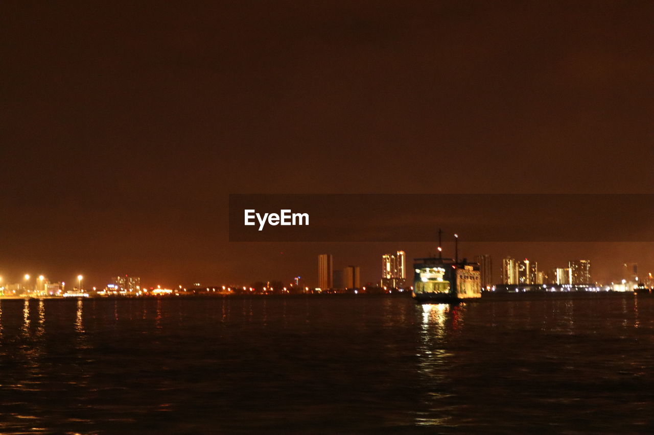 ILLUMINATED BUILDINGS IN SEA AGAINST SKY AT NIGHT