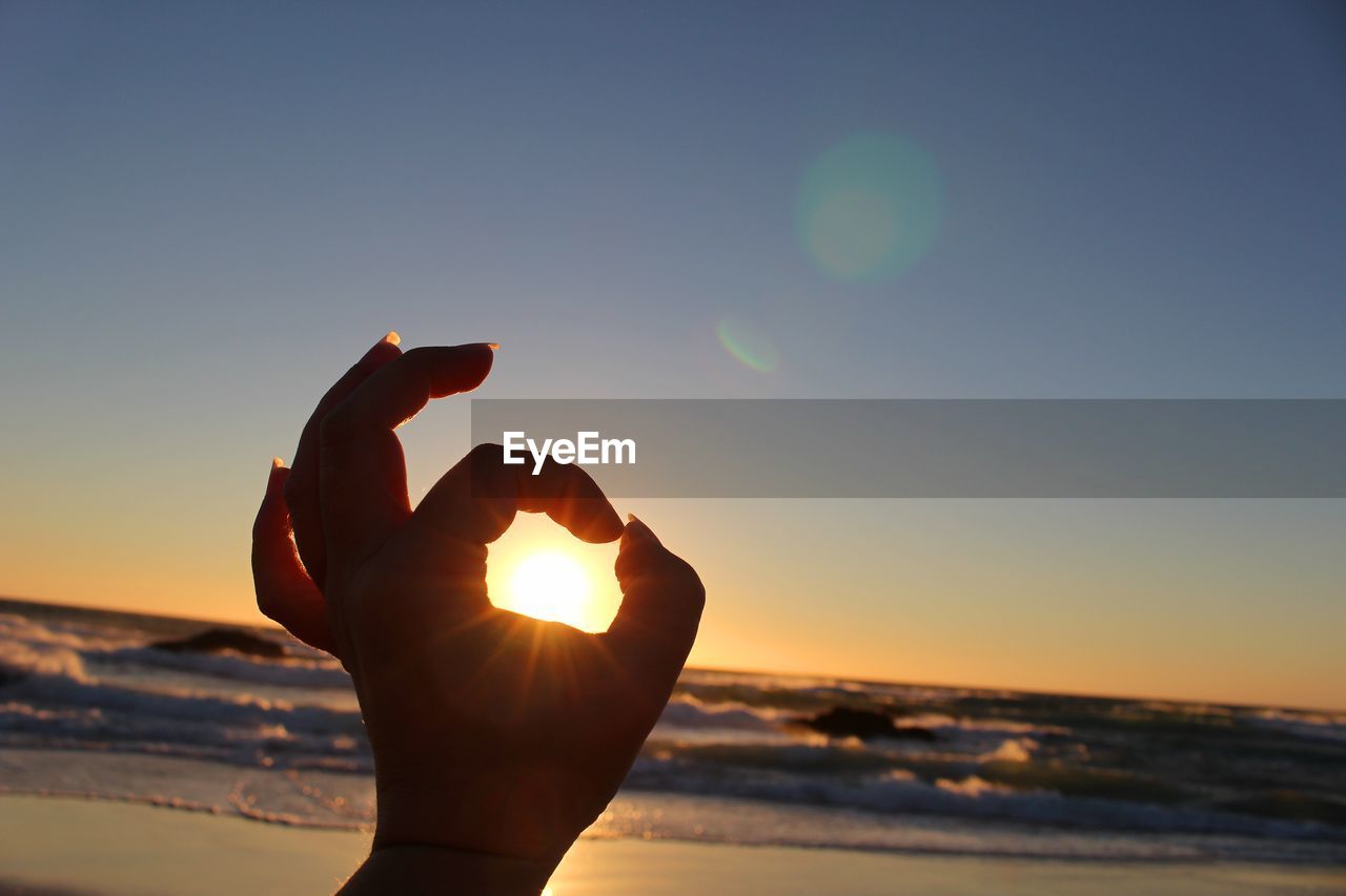 Optical illusion of hand holding sun at beach