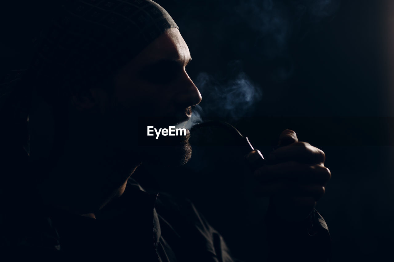 Side view of young man smoking cigarette against black background