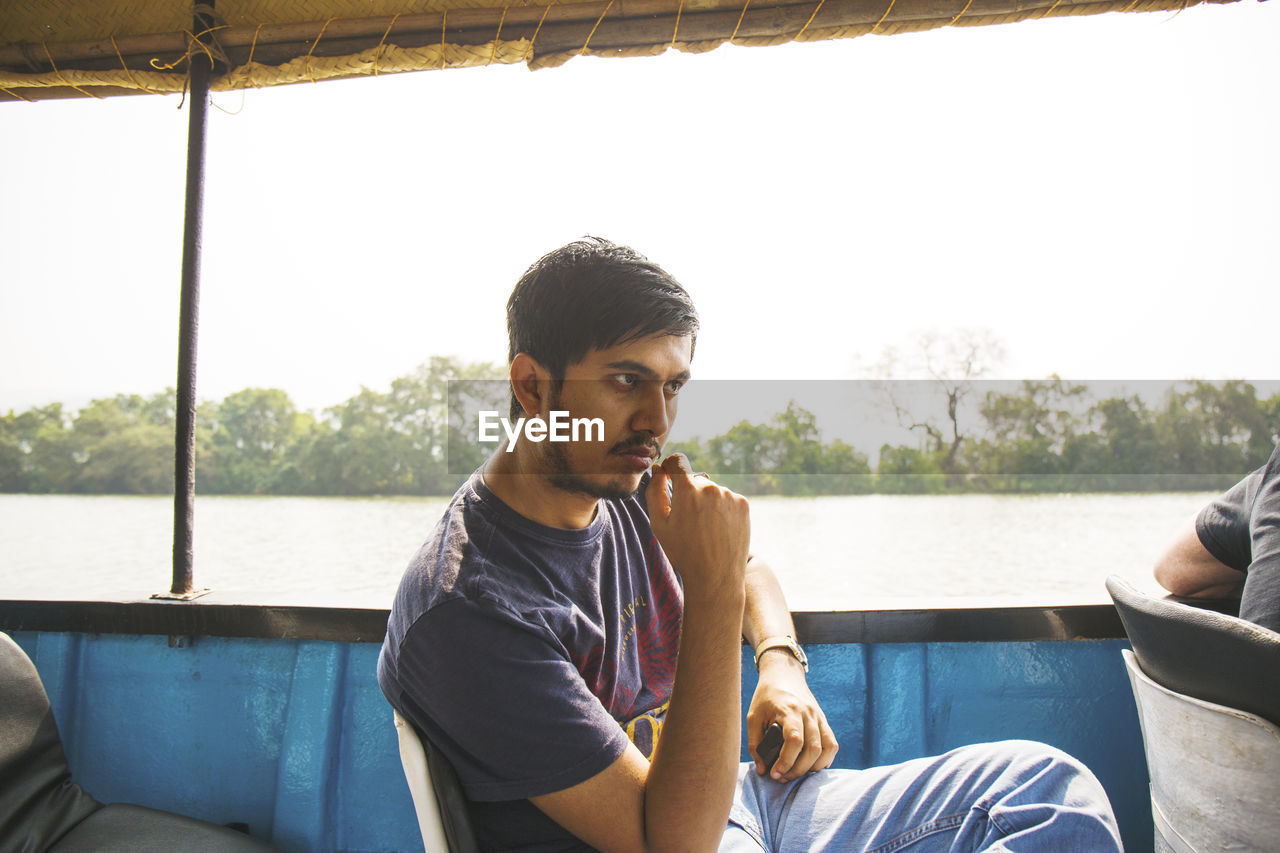 Young man sitting in boat on lake against sky