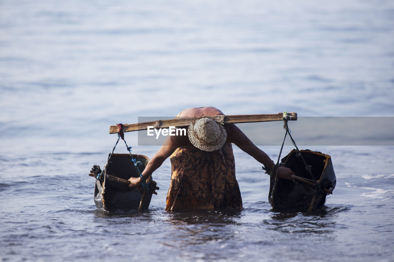 Shirtless man filling water in containers from lake