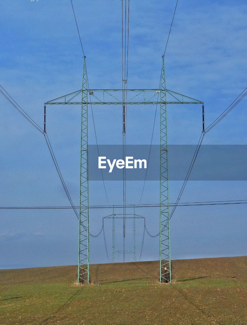 Low angle view of electricity pylon on field against sky