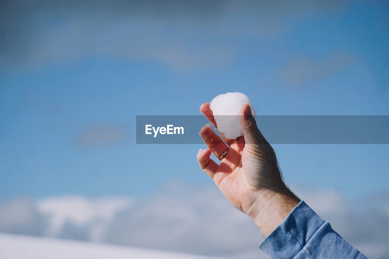 Close-up of person hand holding a snowball against sky