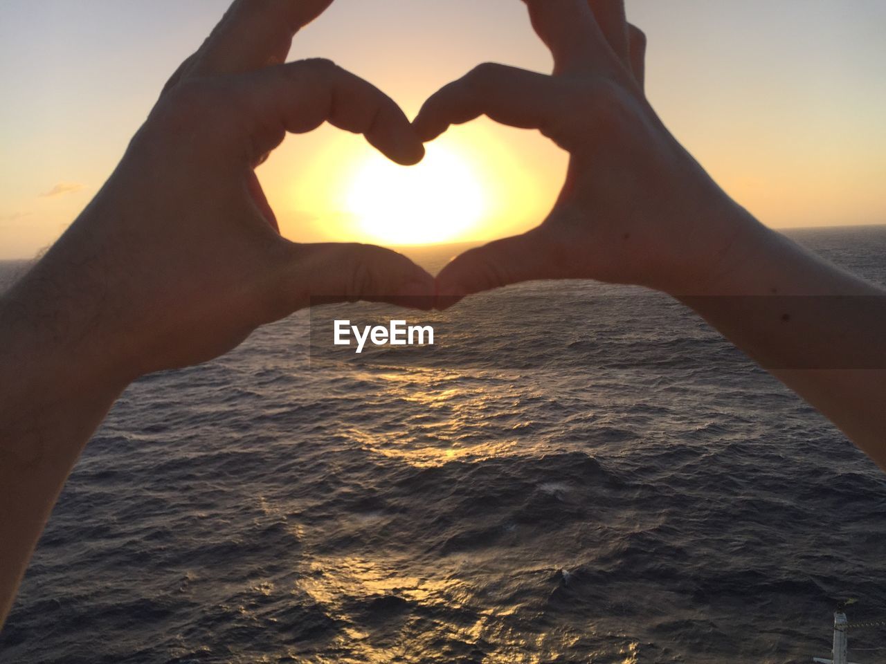 HAND HOLDING HEART SHAPE IN SEA AGAINST SKY
