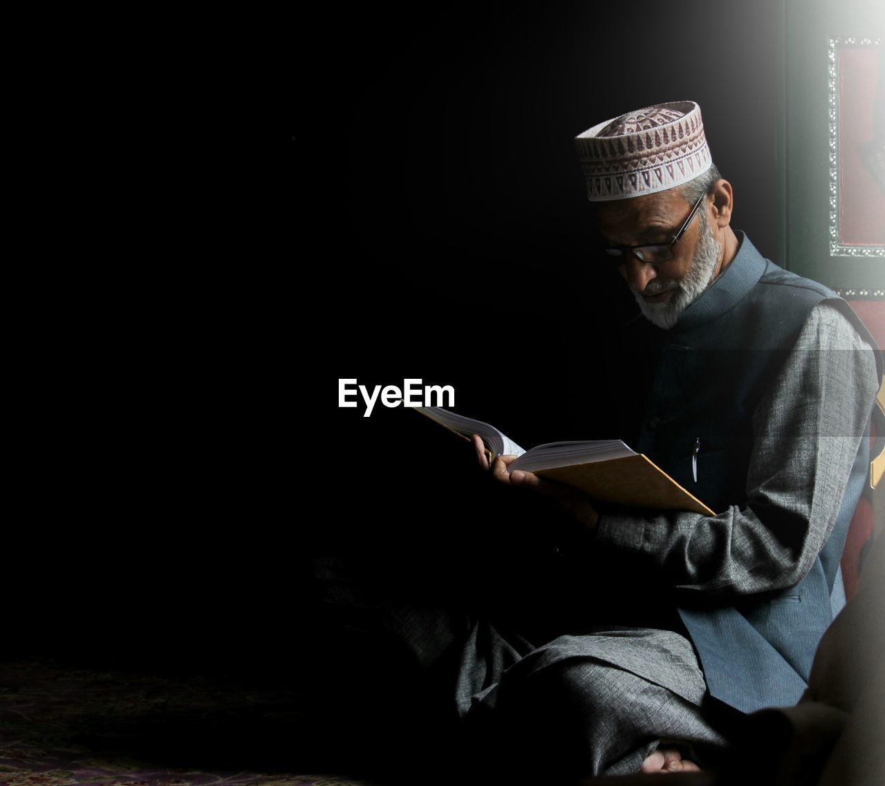 MIDSECTION OF MAN HOLDING MOBILE PHONE WHILE SITTING ON BOOK