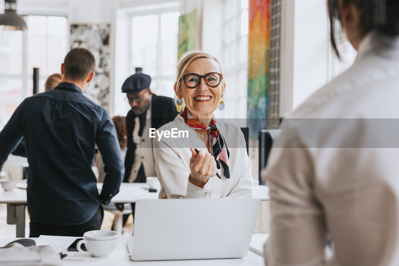 Happy businesswoman wearing eyeglasses discussing with colleague at office