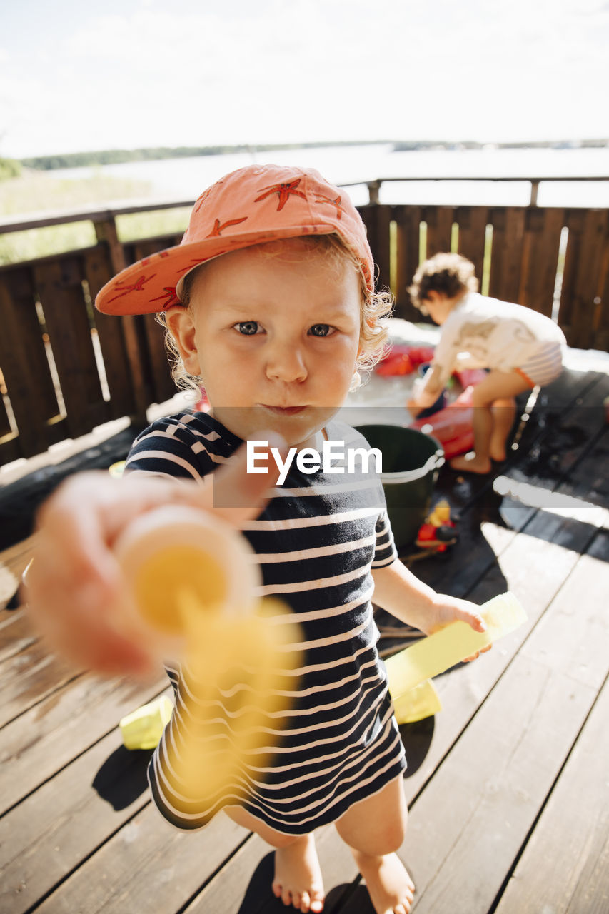 Portrait of cute boy giving toy while standing outdoors during sunny day