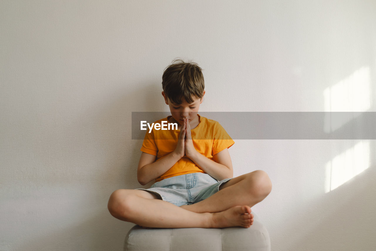 A boy in an orange t-shirt prays at home. concept for faith