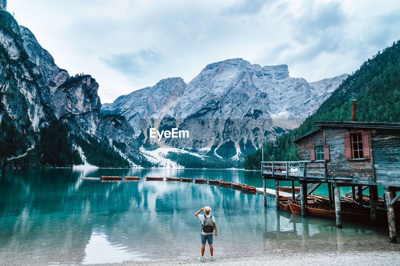 Back view of anonymous male explorer with backpack standing on shore of crystal clear lake with turquoise water and enjoying scenery of mountains during vacation