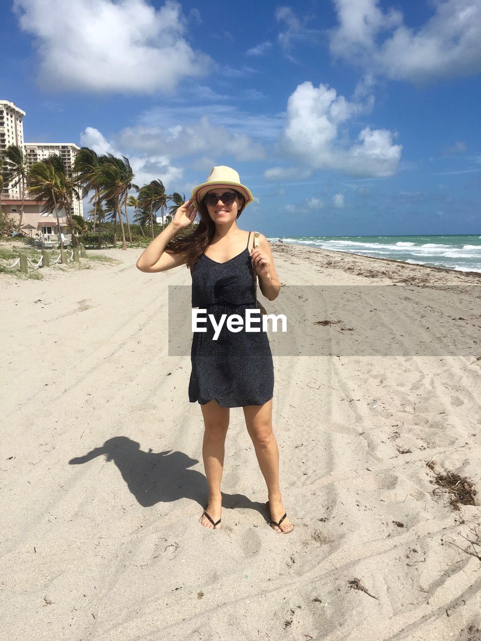 Full length of smiling young woman standing on sand at beach during sunny day