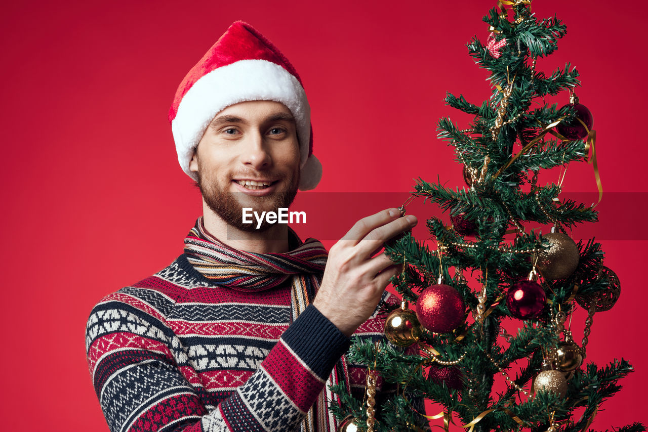 PORTRAIT OF SMILING YOUNG WOMAN WITH CHRISTMAS TREE IN RED DURING WINTER