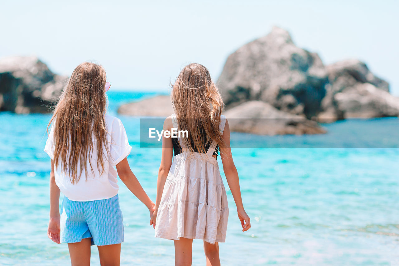 REAR VIEW OF FRIENDS STANDING ON BEACH