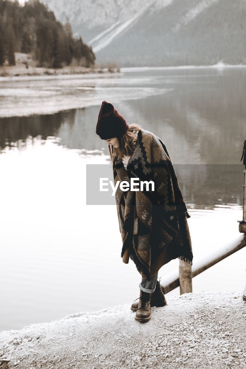 Close-up of young woman standing on rock by lake during winter