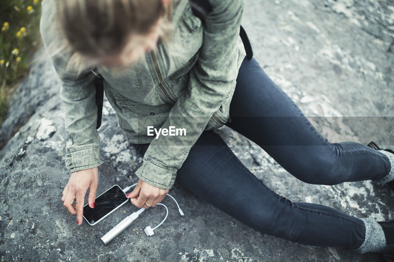 High angle view of woman connecting portable charger to smart phone on rock
