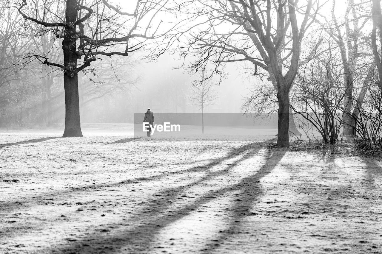 REAR VIEW OF MAN WALKING ON SNOWY LAND