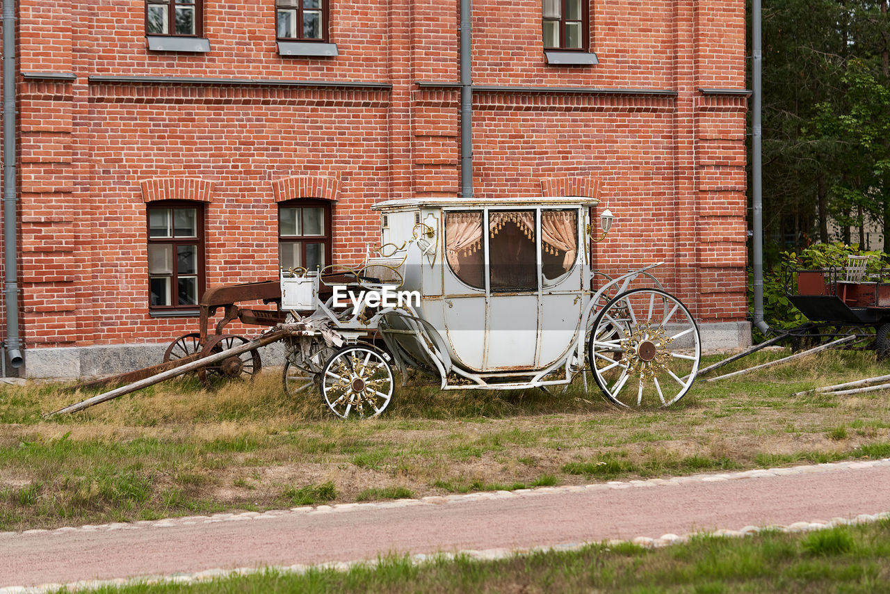 architecture, transportation, building exterior, built structure, transport, vehicle, mode of transportation, carriage, no people, land vehicle, day, building, plant, house, grass, window, city, nature, wheel, bicycle, outdoors, home, cart, street, residential district, rural area, brick, old, brick wall, horse and buggy