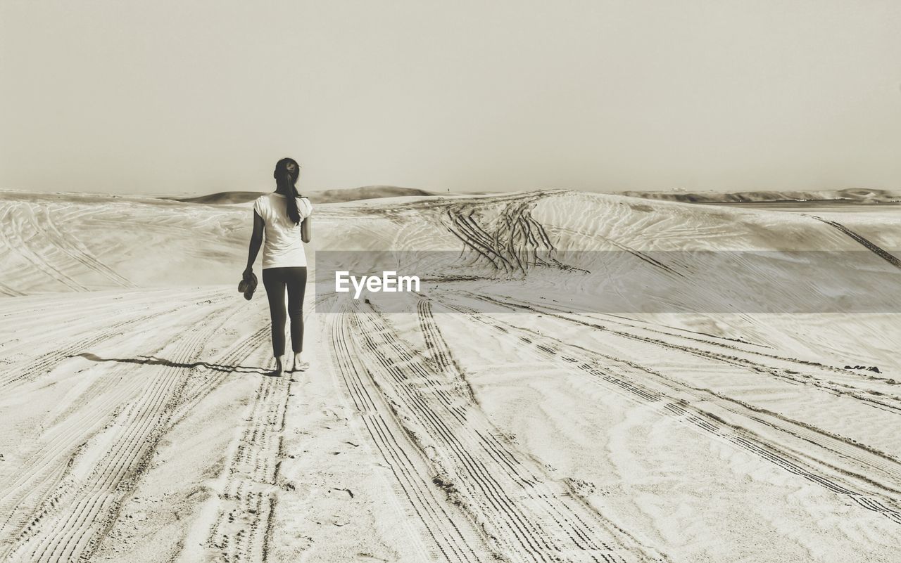 Full length rear view of woman walking on sand in desert