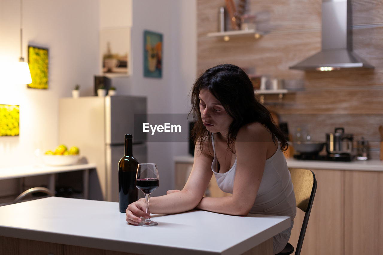 Young woman using phone while sitting on table at home