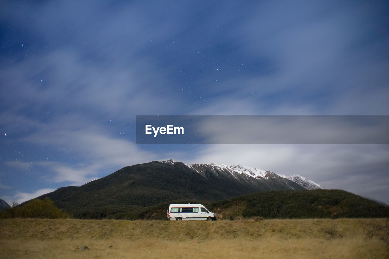A motorhome park at the campsite in new zealand during night with snowcapped mountain in background.