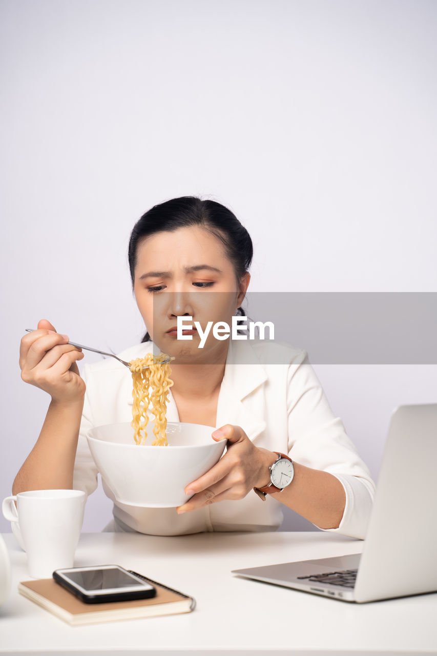 YOUNG WOMAN USING MOBILE PHONE WHILE SITTING IN KITCHEN