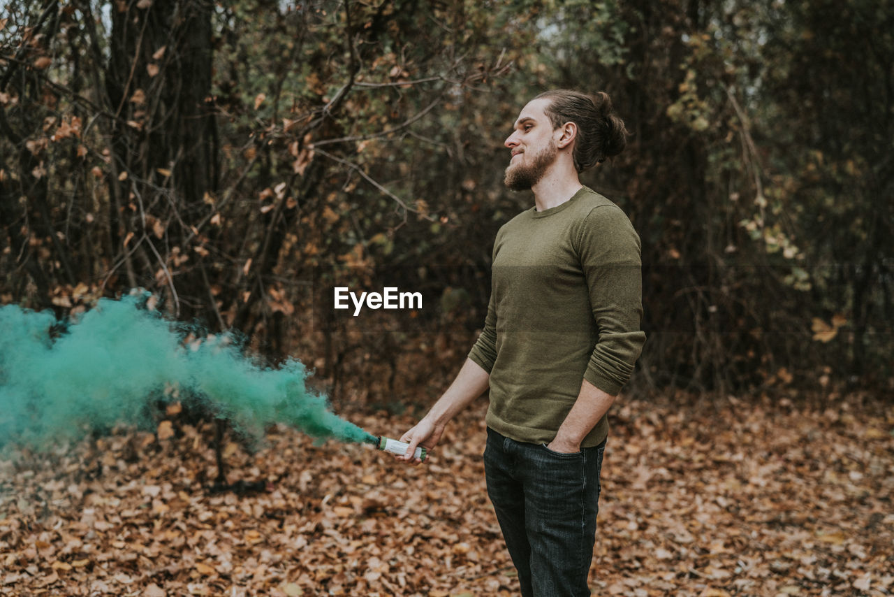 Young man holding distress flare while standing in forest during autumn