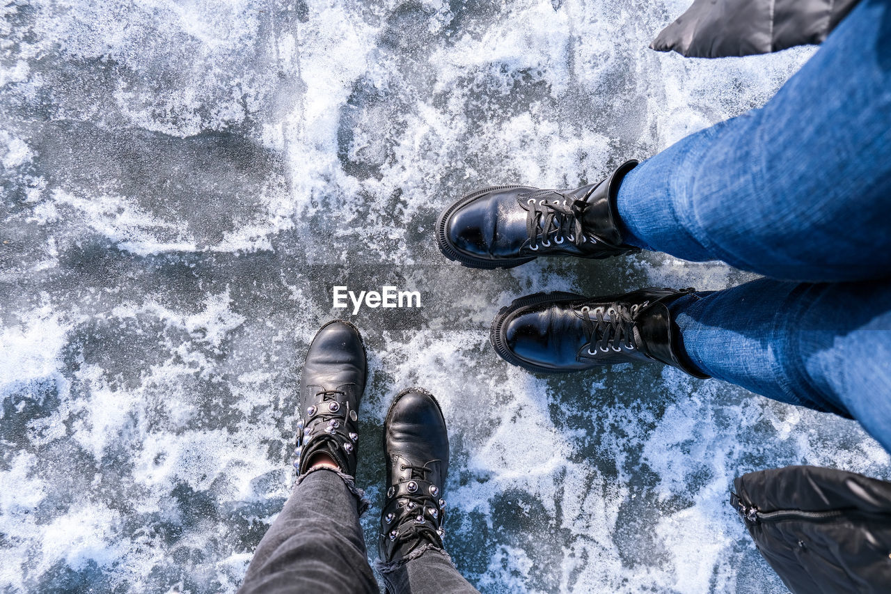 Two girls looking down at feet. frozen lake or river. feet on ice. wearing snow shoes and standing 