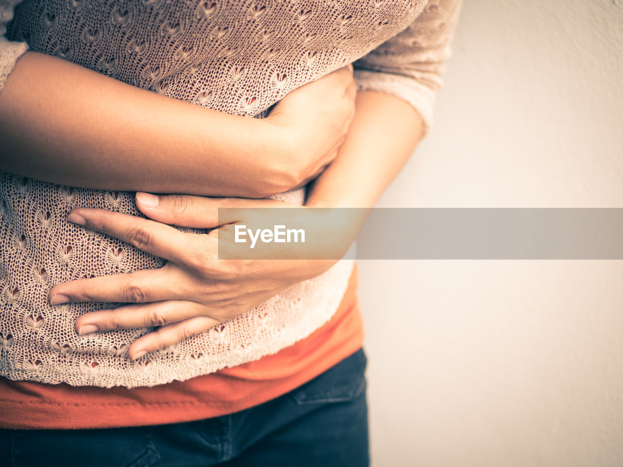 Midsection of woman with stomachache standing against beige background