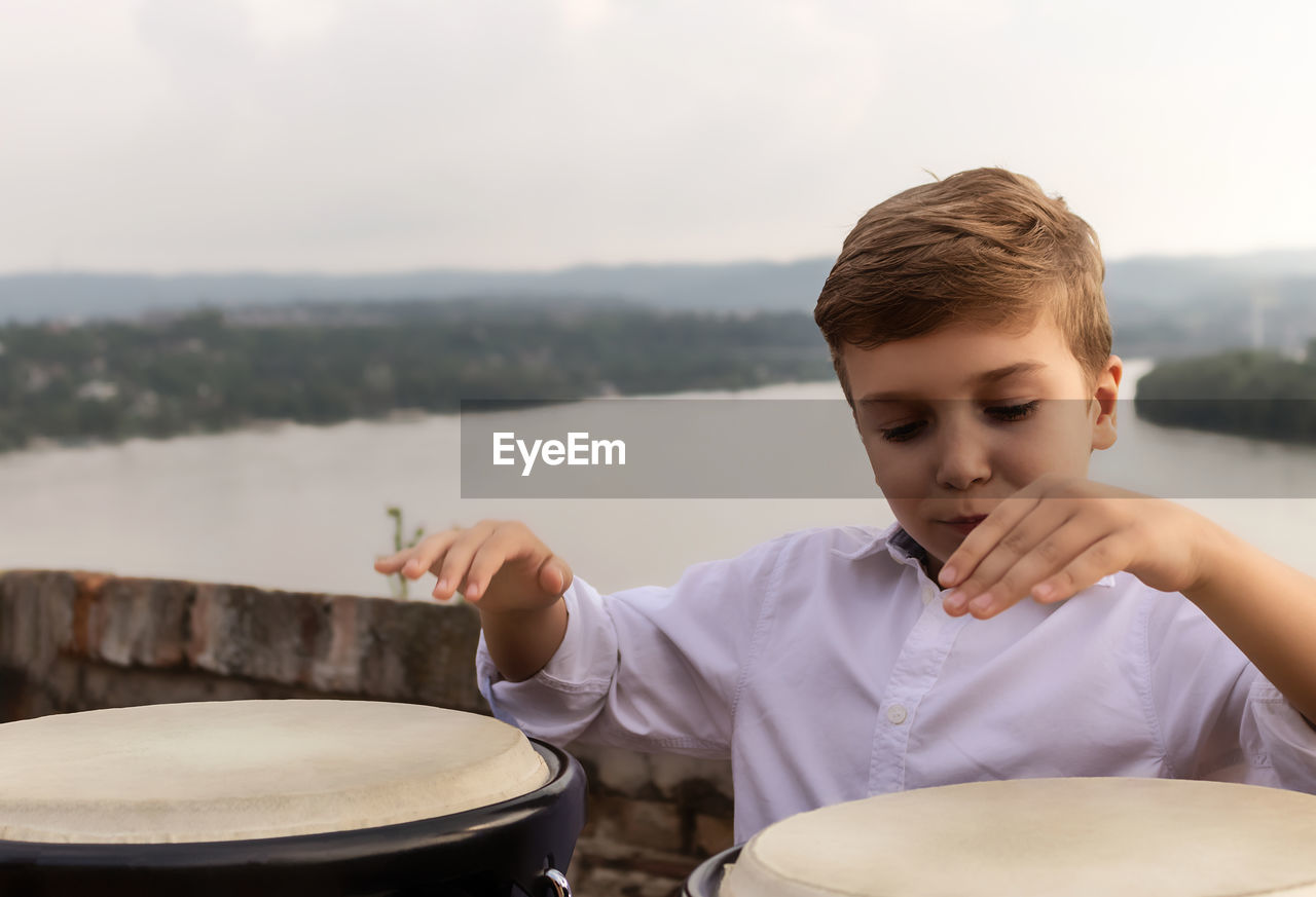 Little drummer playing bongos at riverside.