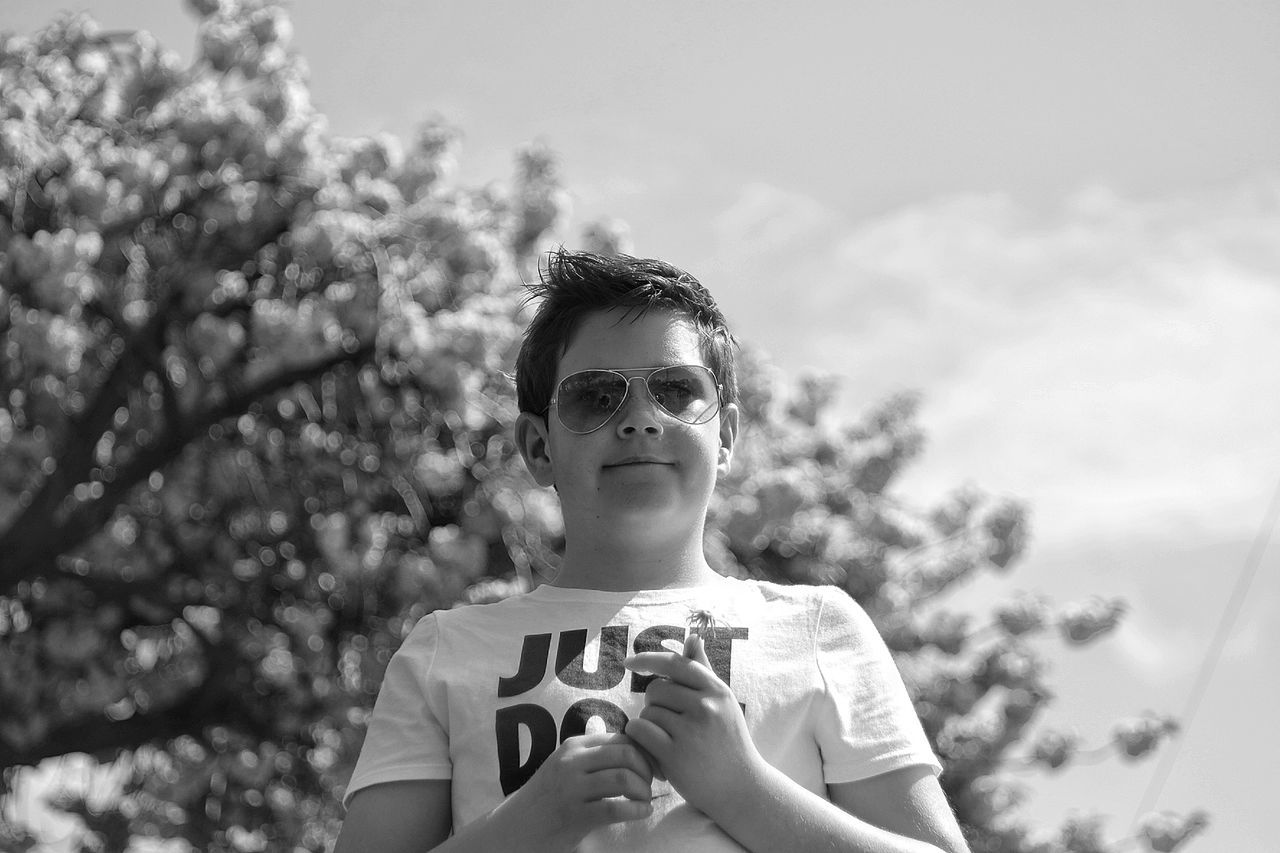 Low angle view of boy wearing sunglasses while standing against sky