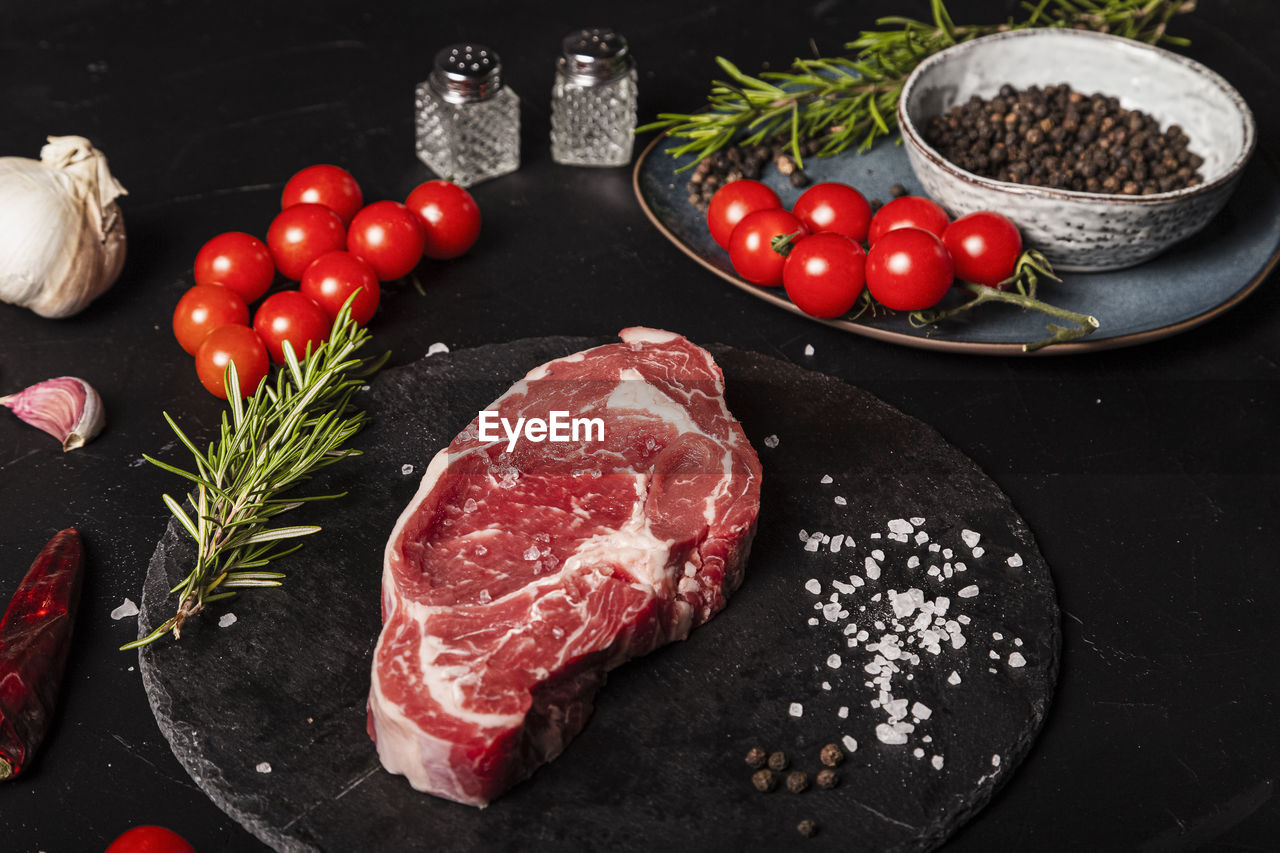 At the table, a raw beef entrecote with rosemary, salt and pepper on a round slate.