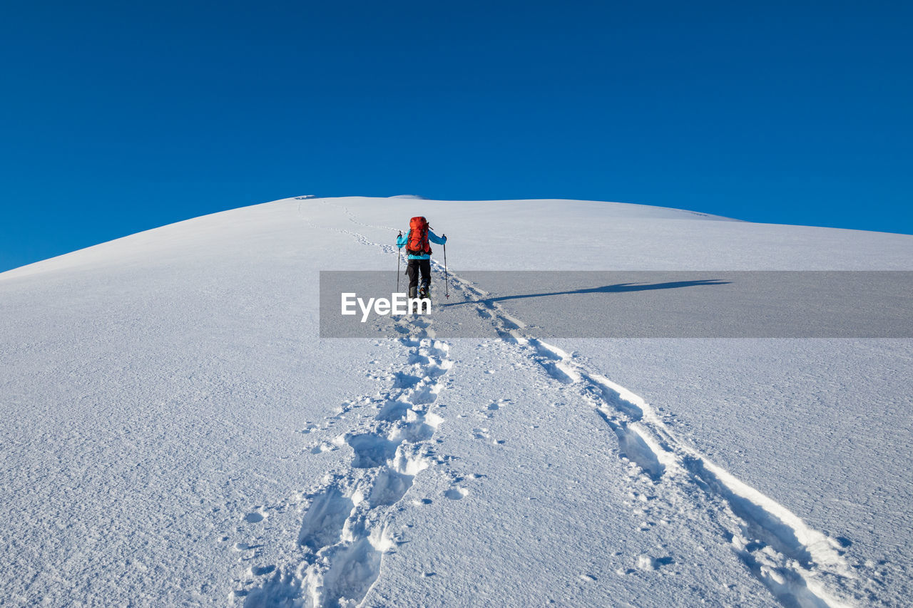 Rear view of person climbing on snowcapped mountain against clear sky