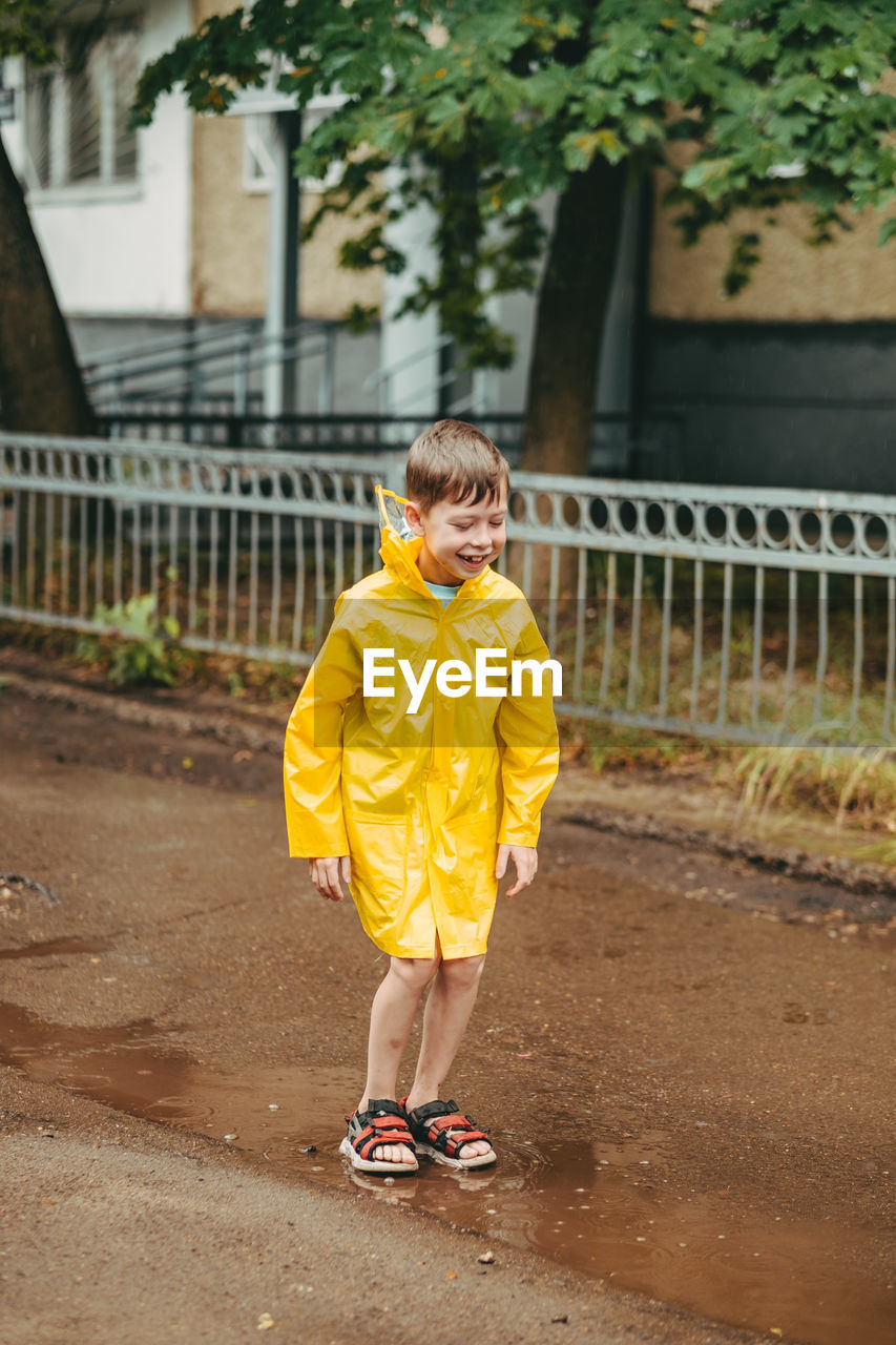 A boy in a yellow raincoat walks outside in the rain. a child jumps on the narrows. 