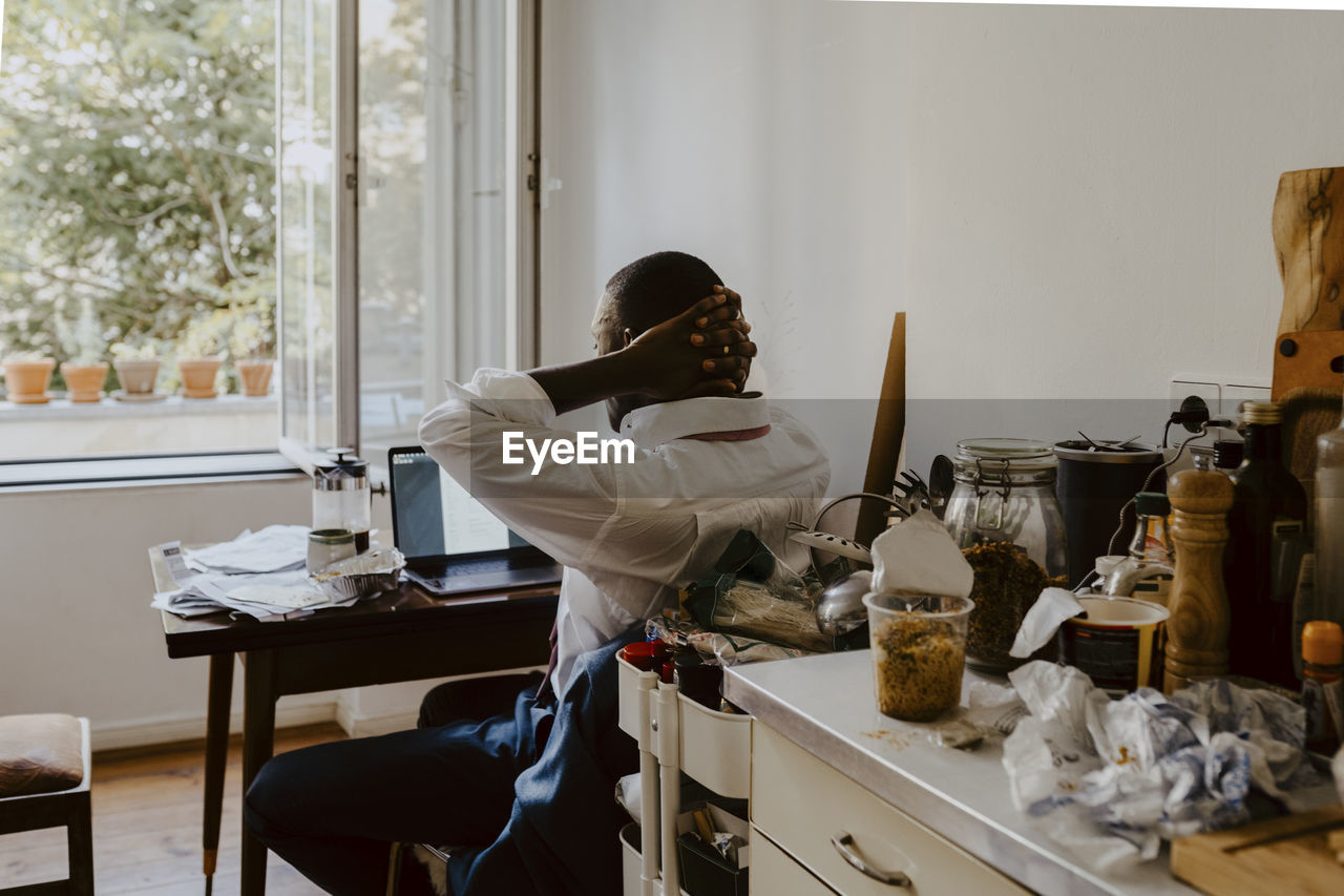Rear view of male entrepreneur with hands behind head in living room