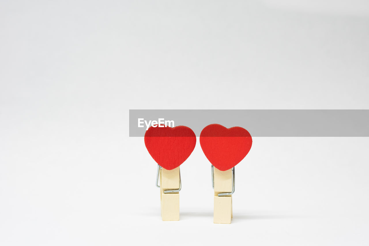 Close-up of red heart shape with clothespins against white background