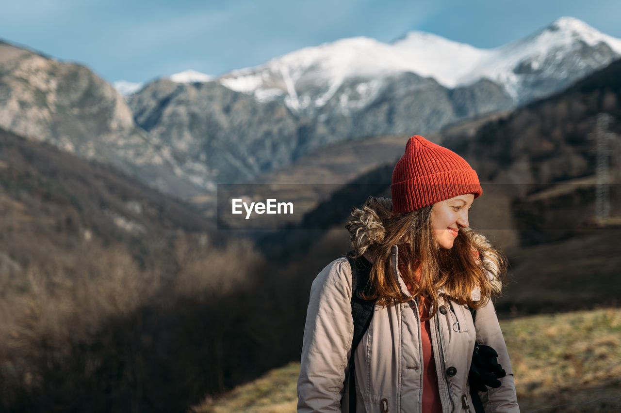 Smiling traveler at the snowy mountains. happy woman in red cap warming up and enjoying the sunlight