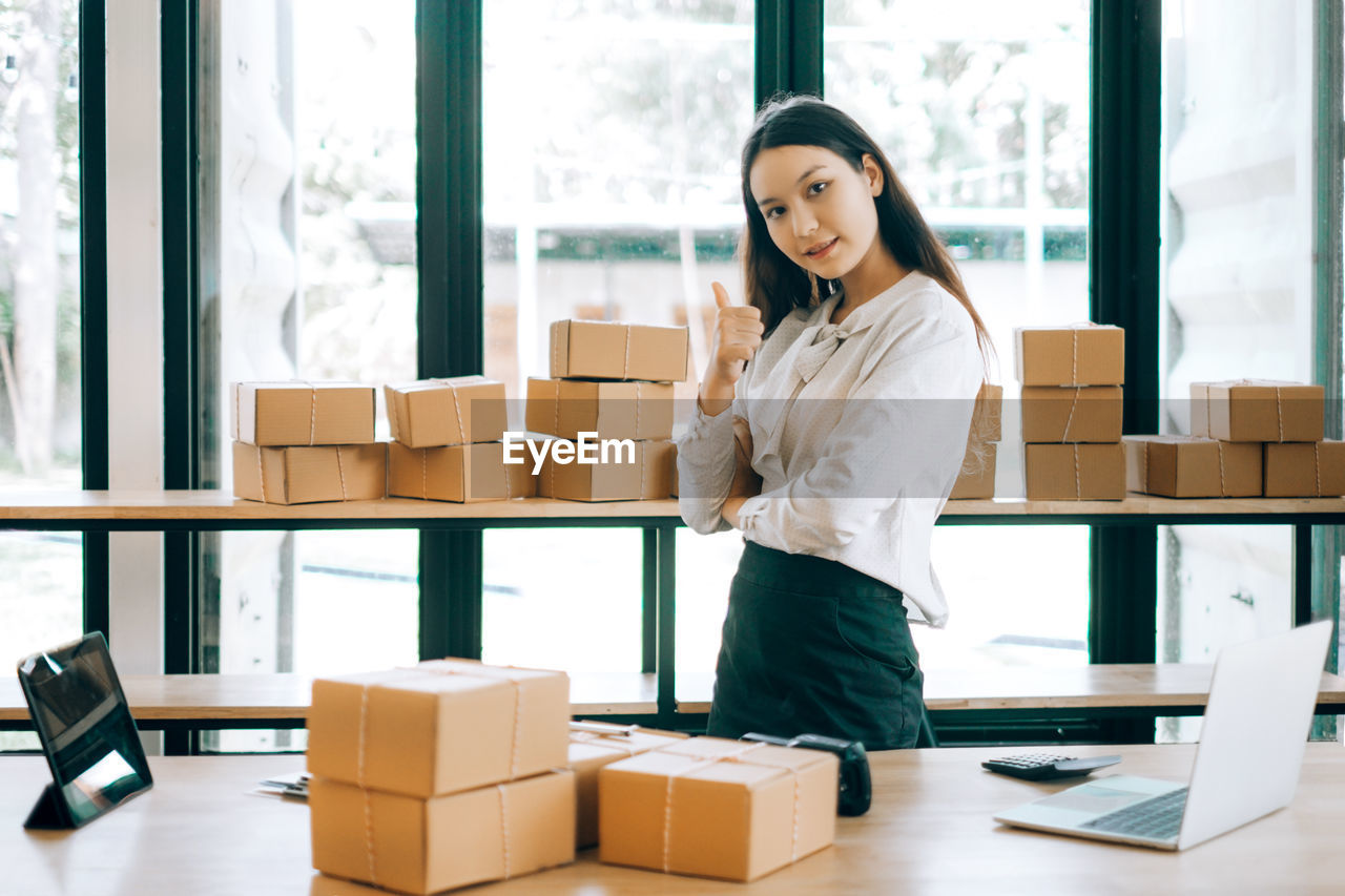 Portrait of young businesswoman standing by packages at office