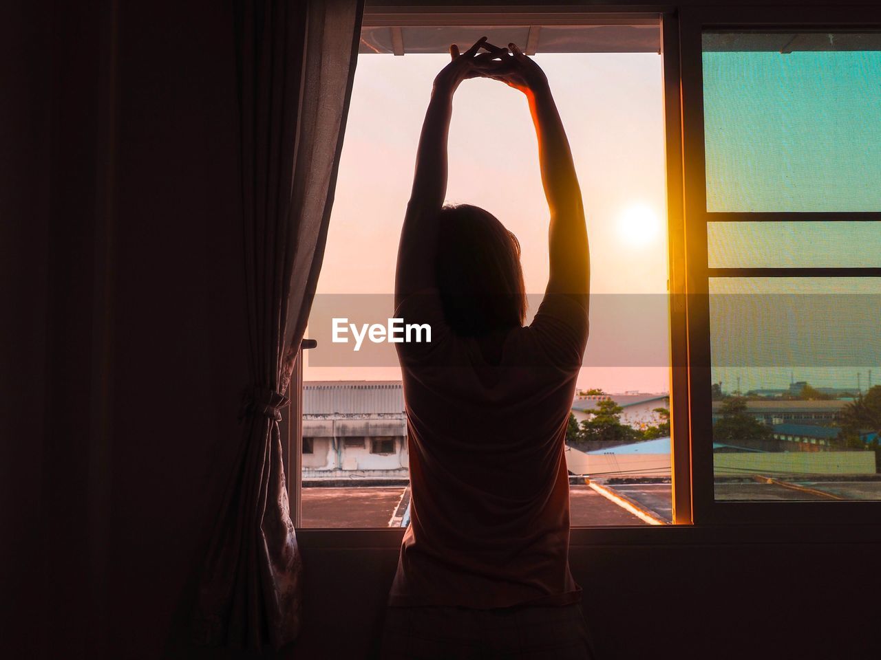 Rear view of woman stretching hands against window