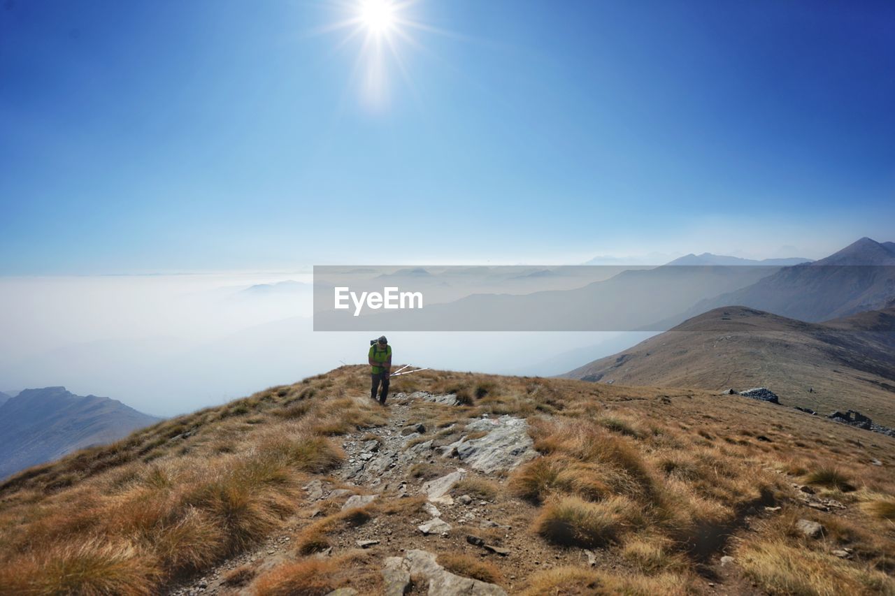 Hiker walking on mountain against blue sky