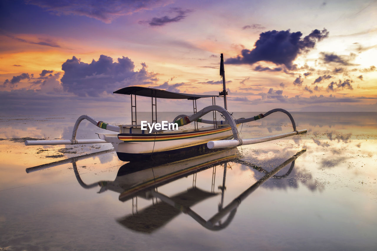 Out trigger boat moored in sea against sky during sunset