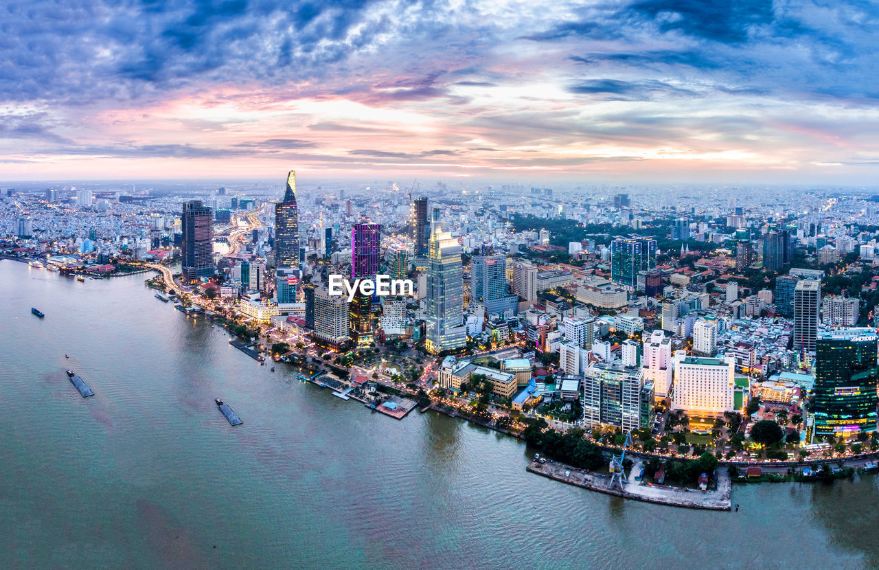 Aerial view of cityscape by river against cloudy sky during sunset